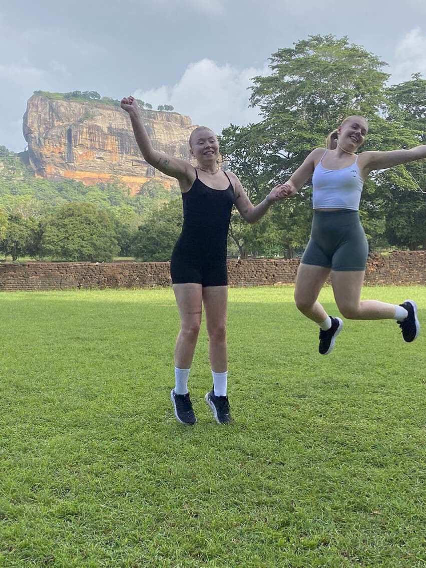 Two travellers jumping on the lawn below Sigiriya rock