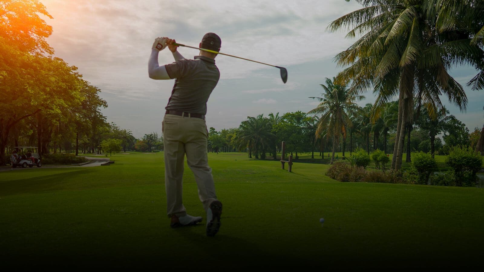 A golfer driving from the tee on a palm-lined course